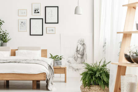 Book placed on a wooden bedside table with plant in grey material pot standing in bedroom with posters on the wallの写真素材