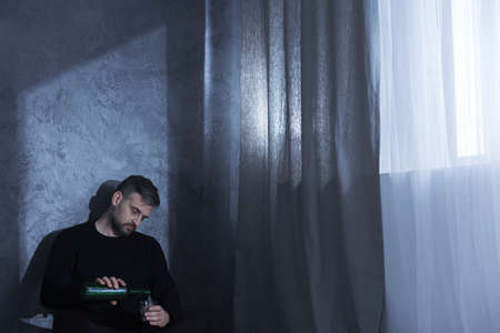 Man with a beard sitting alone in a dark room drinking alcoholの写真素材