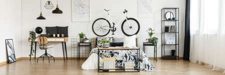 Plants on bedside cabinets and bike on bedhead of king-size bed in spacious bedroom with workspaceの写真素材