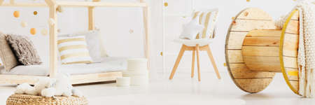 Panorama of simple bright baby room in open white apartment with cozy pillows on DIY bed and large...