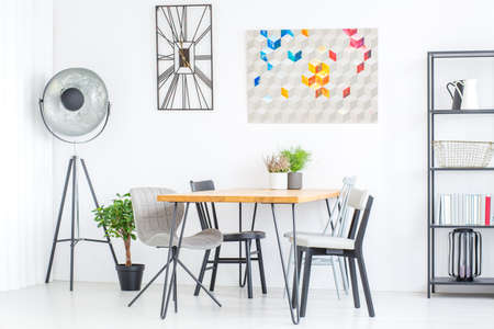 Designer lamp near wooden table with plants in dining room with chairs, poster and clockの写真素材