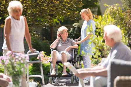 Senior woman in wheelchair spending time outside, getting some fresh air with her nurse from rest...