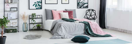 Dark green pillow on the floor in bright bedroom with pink pillows on king-size bed next to a shelf...
