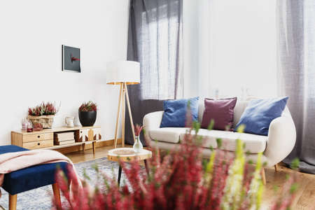 White lamp next to settee with blue pillows under a window in living room interiorの写真素材