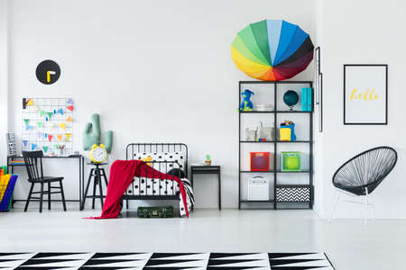 Rainbow umbrella placed on a black metal rack standing in a white room with bed for kidの写真素材