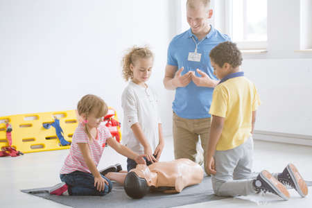 Kindergarten kids practicing first aid steps on a medical dummy with young paramedic