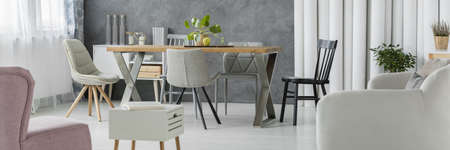 Panorama of open space dining room with wooden table, white sofa and pastel pink armchairの写真素材