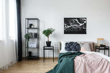 Black and white map poster hanging over pastel pink bed with green blanket in feminine bedroom...