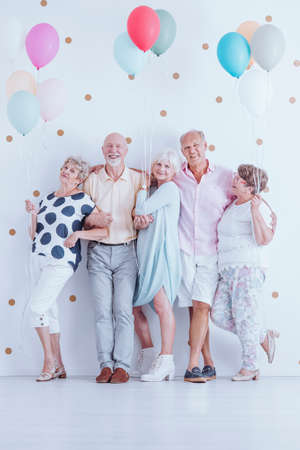 Group of enthusiastic senior friends with colorful balloons celebrating birthdayの写真素材