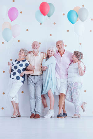 Group of enthusiastic senior friends with colorful balloons celebrating birthday