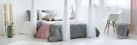 Flowers in vase next to canopy above bed with pink blanket in bedroom with white chair