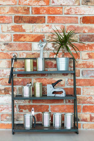 Plant in metal bucket and tools in metal cans on shelf against red brick wall in handyman's roomの写真素材