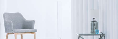 Comfortable chic chair standing in an apartment living room interior next to a glass table with lamp, and a blue glassの写真素材