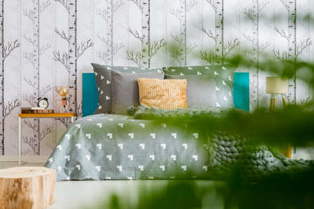 Bright bedroom with forest wallpaper in the photo with plant in blurred foregroundの写真素材