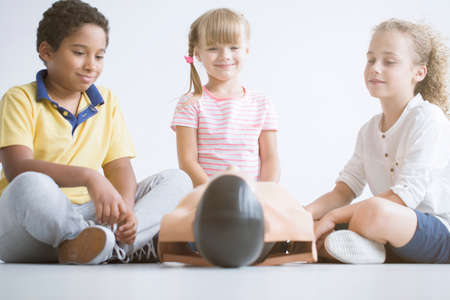 Smiling girl and afro-american boy practicing first aid on a manikinの写真素材