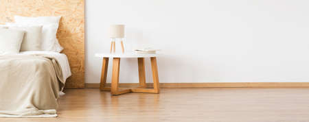 Lamp on wooden table near bed with pillows against white wall with copy space in natural bedroomの写真素材