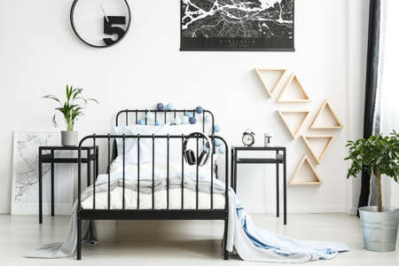 Headphones on bed with bright bedding between nightstands with clock and plant in teenager's bedroom with triangles on the wallの写真素材
