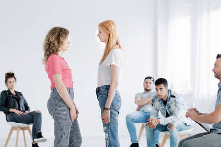 Young girls facing each other during psychotherapy with rebellious teenagers in white office