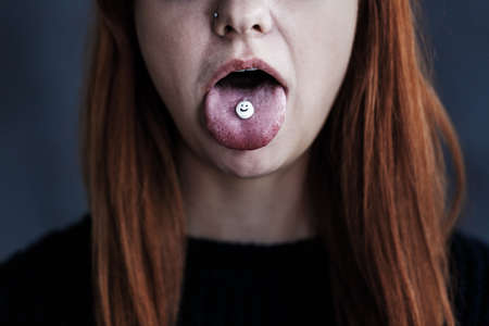 Close-up of the mouth of a rebellious red-haired girl with a pill on her tongueの写真素材
