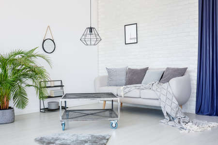 Grey blanket on sofa with cushions against wall with poster in modern living room interior with...