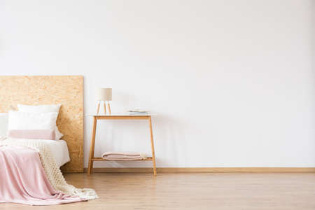 Lamp on wooden table against white wall with copy space in simple bedroom with pink blanket on bedの写真素材