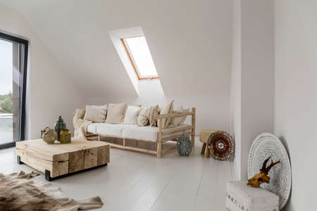 Decorative lantern and vase on wooden table between beige sofa and fur on floor in rustic living roomの写真素材
