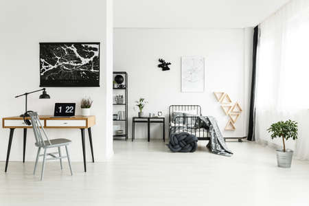 Grey chair at desk with plant and laptop against a wall with black map in teenager's bedroom with moose clock above bedの写真素材