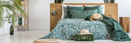 Panorama of wooden bed with green bedsheets with floral pattern and vintage camera hanging on the...