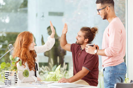 Man and colleagues high five during work in the open space of corporation