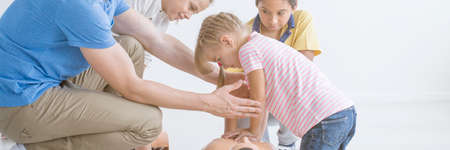Boy pressing chest of a manikin and trainer supporting him during first aid trainingの写真素材