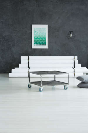 Industrial metal table and grey pillows in living room with green poster above designer sofa