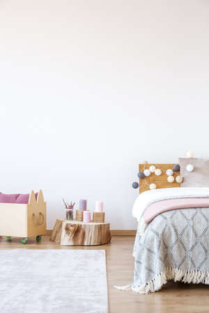Candles on a wooden stump next to a crate and cotton balls on bed in bright bedroom with copy space on a wallの写真素材