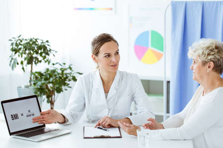 Dietitian telling a patient about BMI using a laptop on desk in the officeの写真素材