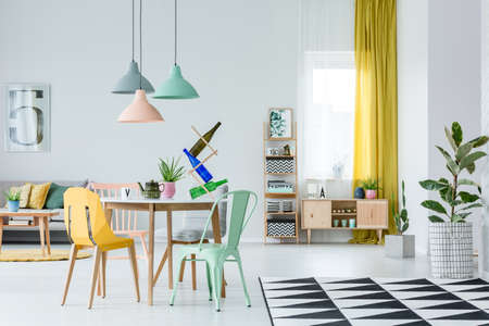 Plant on geometric carpet and rustic cupboard in cozy living room interior with yellow and mint...