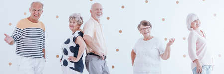 Smiling senior friends posing and enjoying retirement together. White wall with gold dots in the backgroundの写真素材