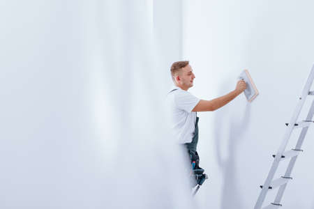 handyman cleaning white wall using wiper during finishing interior with ladderの写真素材