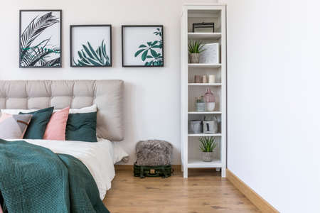 White cabinet next to bed with green pillows against the wall with gallery of posters in bedroom interiorの写真素材