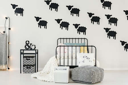 Black sheep stickers on the wall in bright bedroom for a baby with loudspeaker and patterned pouf...