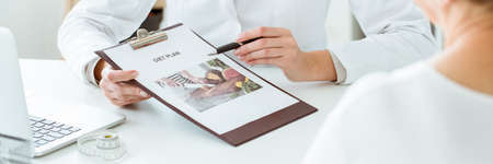 Close-up of nutritionist holding a diet plan personalized for a diabetic. Laptop and measure tape on...