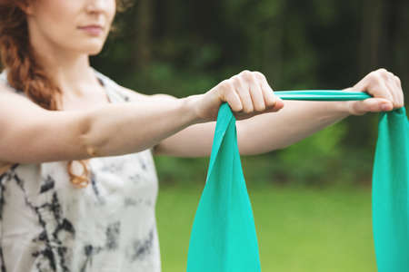 Young woman exercising with green stretch band outdoors, in the garden