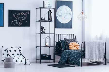 Orange knot pillow on the bed next to shelves in astronaut's bedroom interior with poster of the...