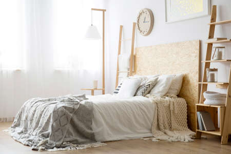 Side angle of white bed with wooden bedhead and gray blanket in bright bedroomの写真素材