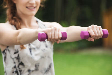 Smiling attractive woman with red hair holding dumbbells in the parkの写真素材