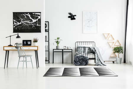 Black and white carpet between wooden workspace with laptop and bright bedroom with knot pillowの写真素材