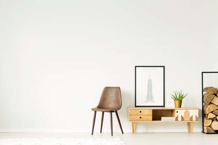 Rustic cupboard with poster and plant between brown chair and wood logs in natural living room interior with copy spaceの写真素材