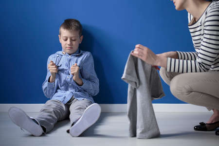 Mother taking care of kid with Heller syndrome sitting on the floor against blue wallの写真素材