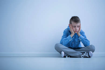 Depressed boy with Asperger syndrome sitting alone against a wall with copy spaceの写真素材