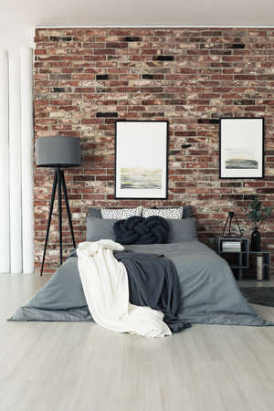 Large grey lamp standing by a bed in a modern brick walled interior of a homeの写真素材