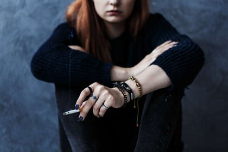 Close-up of rebellious girl wearing black clothes and smoking a cigaretteの写真素材