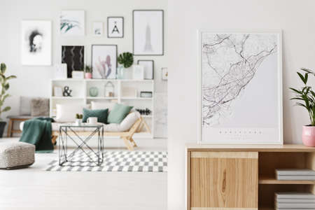 Map and plant on wooden cupboard in the foreground and living room interior with table, pouf and settee in the backgroundの写真素材